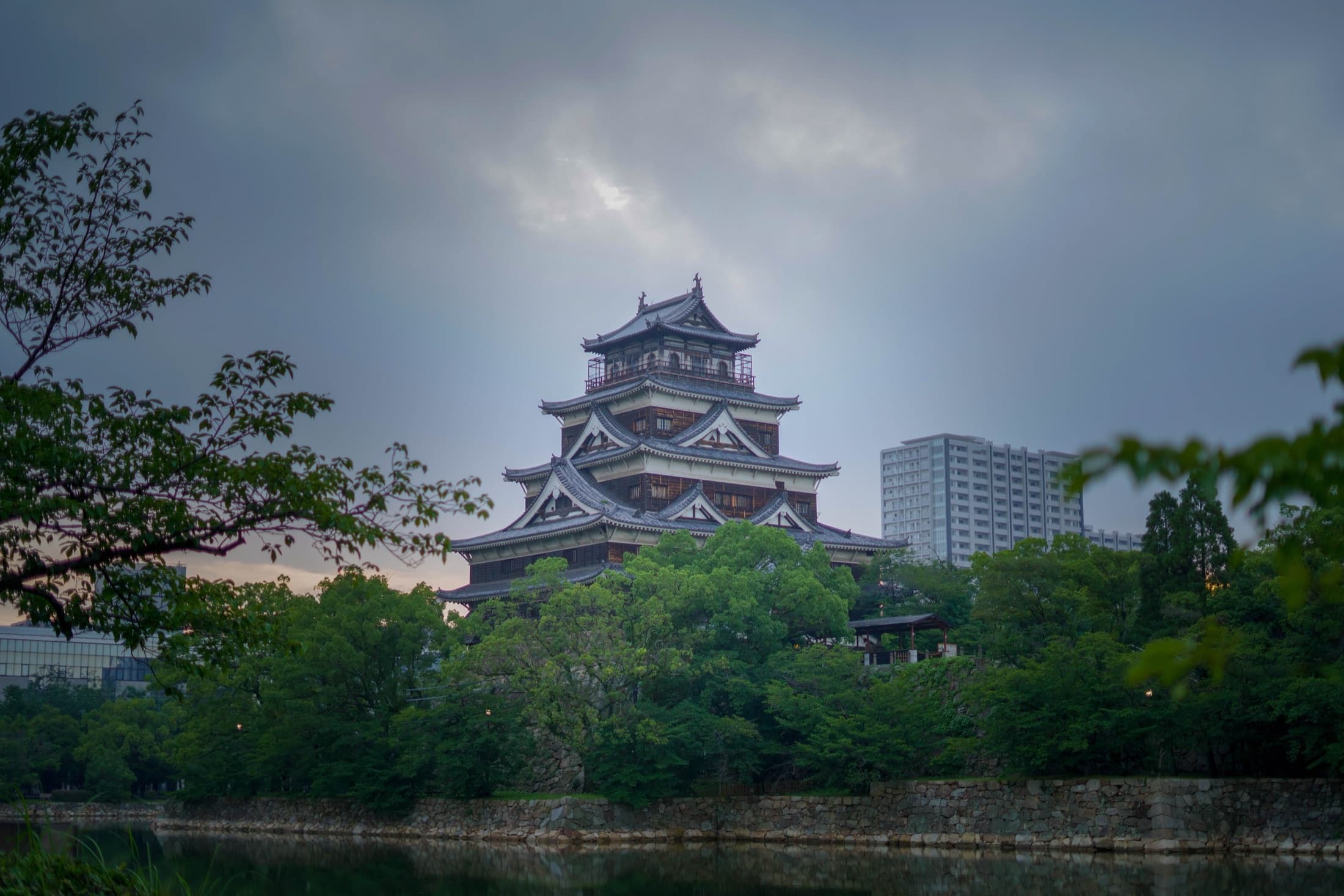 Hiroshima Castle framed by foliage under a heavy sky.