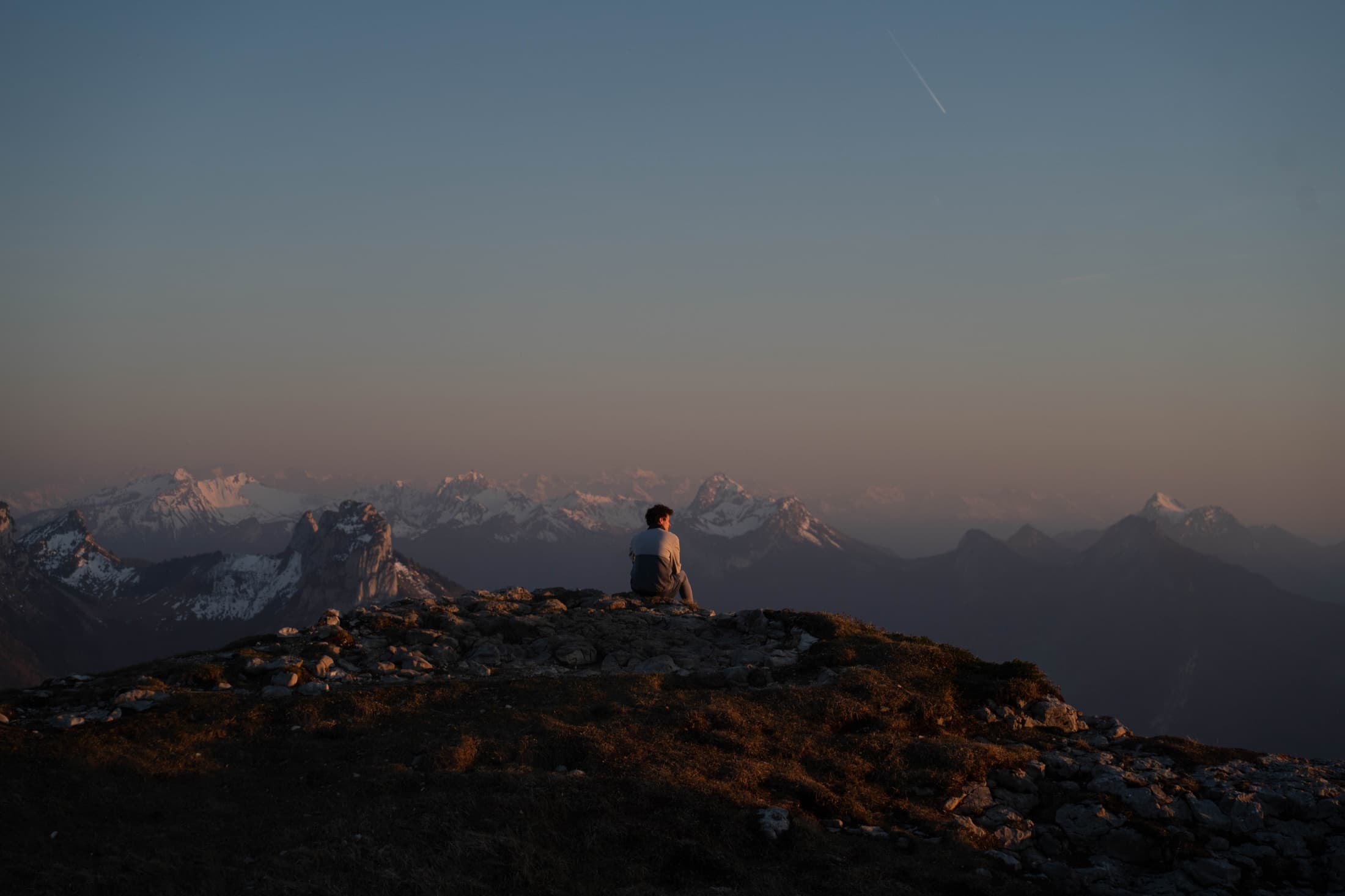 A hiker sitting on a ridge looking out over the Alps at last light.